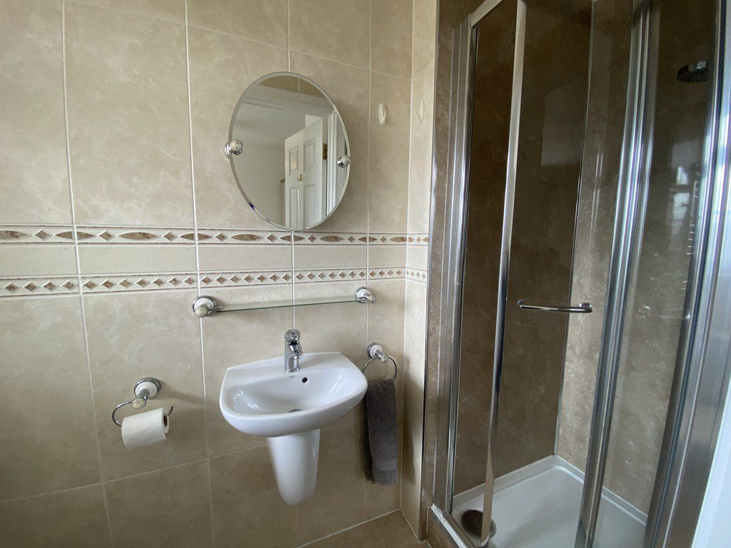 IMG_25_32_largejpg - Sovereign Estates Sovereign Estates Beige tiled bathroom with a white pedestal sink round mirror towel bar and a glass enclosed shower 2026 Beige tiled bathroom with a white pedestal sink round mirror towel bar and a glass enclosed shower