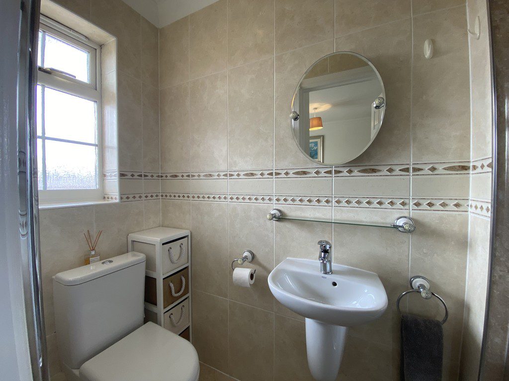 IMG_25_33_largejpg - Sovereign Estates Sovereign Estates Small beige tiled bathroom with a white toilet pedestal sink oval mirror and a window on the left 2026 Small beige tiled bathroom with a white toilet pedestal sink oval mirror and a window on the left