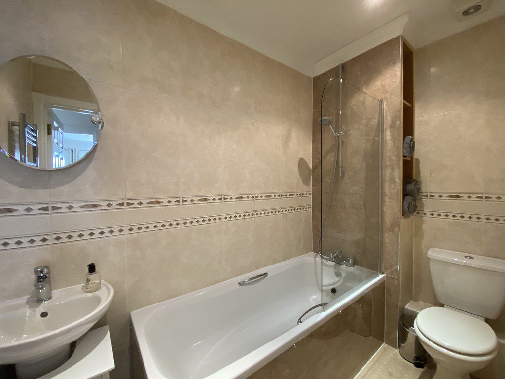 IMG_25_34_largejpg - Sovereign Estates Sovereign Estates Beige tiled bathroom with a white bathtub glass shower screen sink round mirror and toilet with towels on a shelf nearby 2026 Beige tiled bathroom with a white bathtub glass shower screen sink round mirror and toilet with towels on a shelf nearby