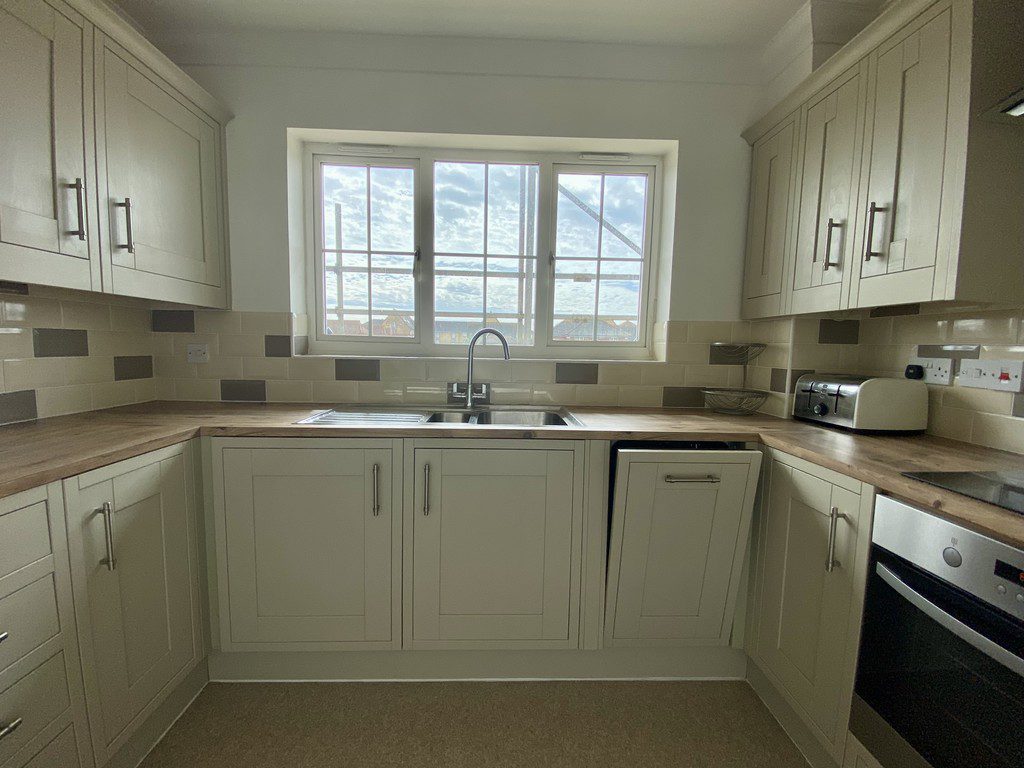 IMG_25_44_largejpg - Sovereign Estates Sovereign Estates White L shaped kitchen with a window above a double sink and wooden countertops Upper and lower cabinets provide storage A toaster and appliance are on the right counter an oven is built in at the far right 2026 White L shaped kitchen with a window above a double sink and wooden countertops Upper and lower cabinets provide storage A toaster and appliance are on the right counter an oven is built in at the far right