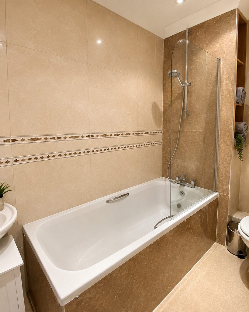 IMG_25_51_largejpg - Sovereign Estates Sovereign Estates Modern beige tiled bathroom featuring a white rectangular bathtub with a curved glass shower screen and chrome fixtures 2026 Modern beige tiled bathroom featuring a white rectangular bathtub with a curved glass shower screen and chrome fixtures